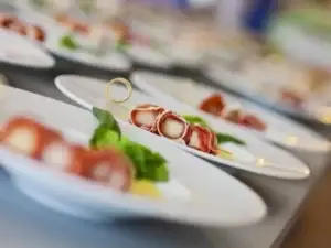 Entrantes de catering en platos blancos: rollitos de jamón con queso y albahaca