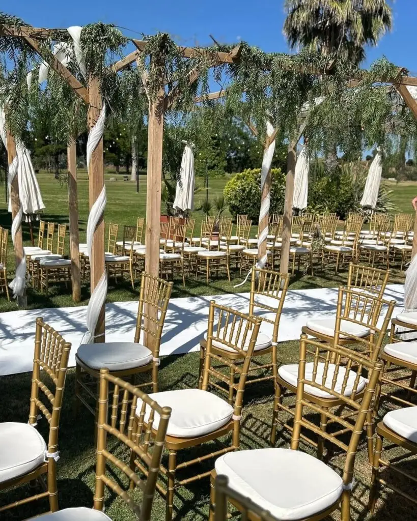 Montaje de ceremonia de boda civil al aire libre en Badajoz con arco de madera y sillas chiavari doradas
