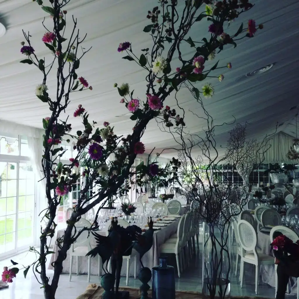 Salón interior decorado con árboles florales y mesa imperial con sillas blancas para un banquete